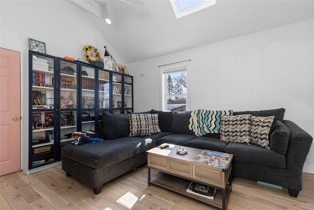 living room featuring a skylight, high vaulted ceiling, and light wood-type flooring