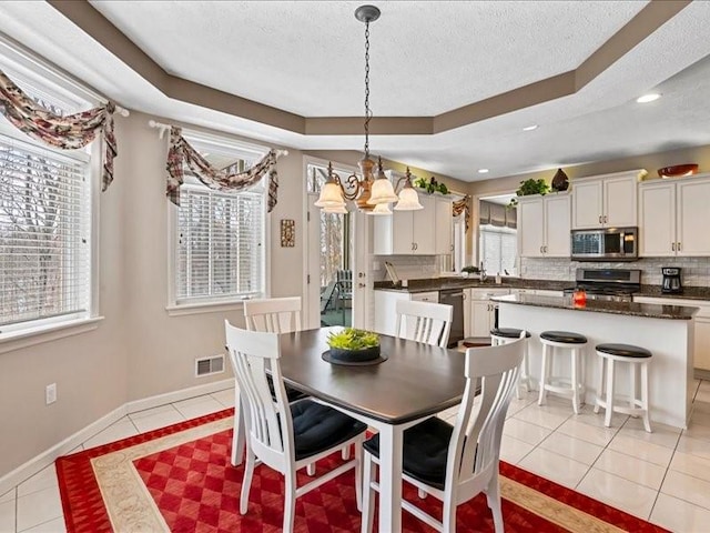 tiled dining room featuring a raised ceiling, a notable chandelier, and a textured ceiling