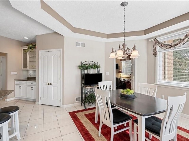 tiled dining room with a textured ceiling, a chandelier, and a tray ceiling