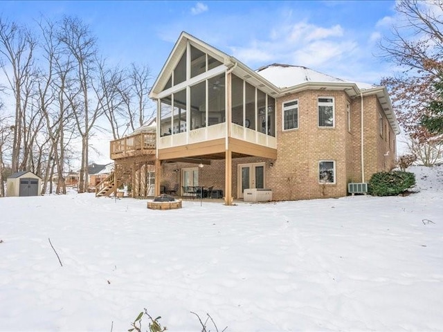 snow covered rear of property with an outdoor fire pit, a deck, and a sunroom