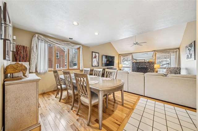 dining room with lofted ceiling, a tile fireplace, ceiling fan, light hardwood / wood-style floors, and a textured ceiling