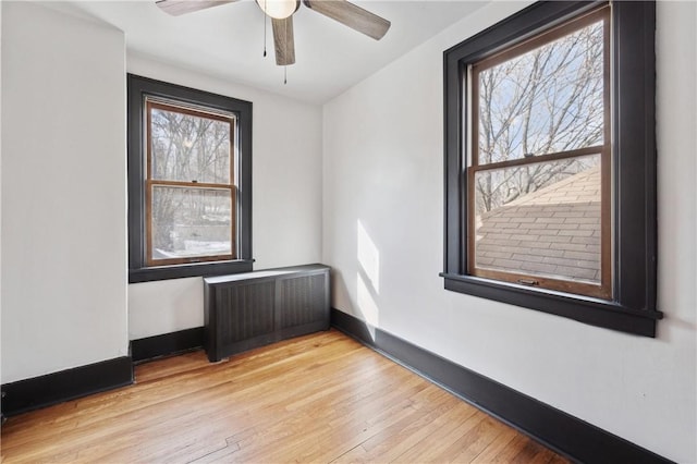 empty room with radiator heating unit, light hardwood / wood-style floors, ceiling fan, and plenty of natural light