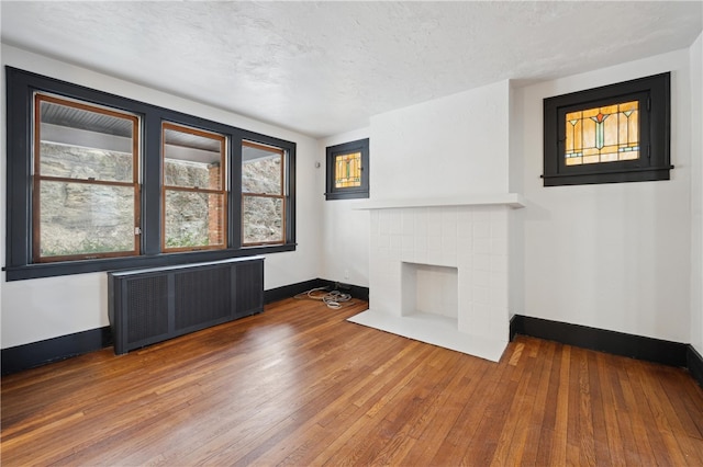 unfurnished living room featuring hardwood / wood-style floors, a tile fireplace, radiator heating unit, and a textured ceiling