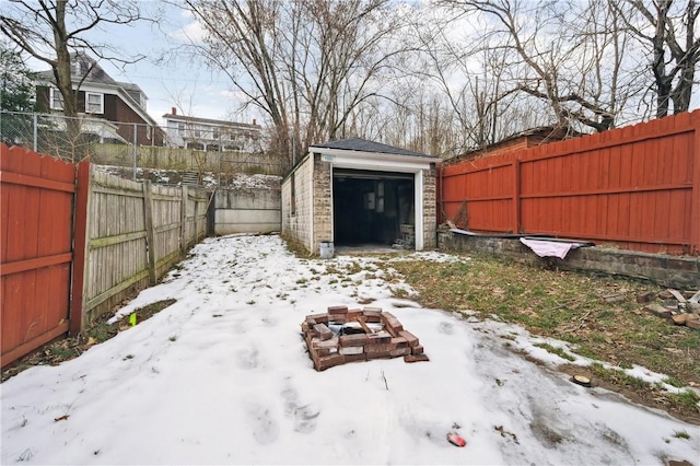 yard layered in snow featuring a garage, an outdoor structure, and an outdoor fire pit