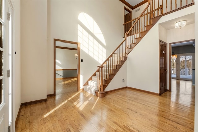 interior space featuring french doors, a towering ceiling, a chandelier, and light hardwood / wood-style flooring