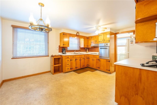 kitchen with sink, hanging light fixtures, backsplash, a healthy amount of sunlight, and oven