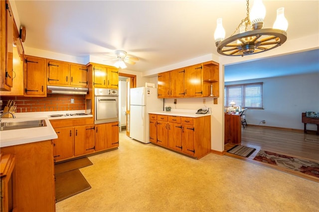 kitchen with sink, decorative light fixtures, white appliances, ceiling fan with notable chandelier, and decorative backsplash