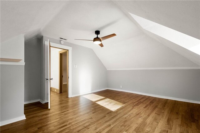 additional living space with ceiling fan, a textured ceiling, wood-type flooring, and vaulted ceiling with skylight