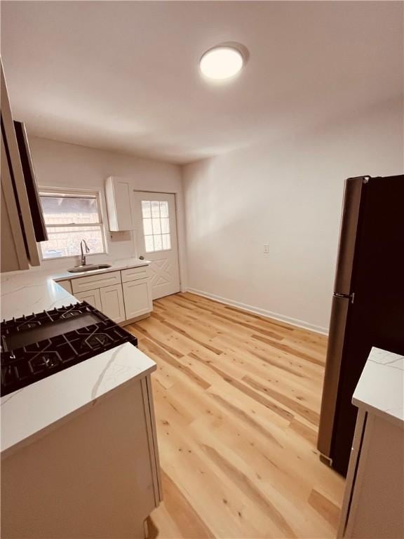 kitchen with sink, stainless steel fridge, white cabinets, and light wood-type flooring