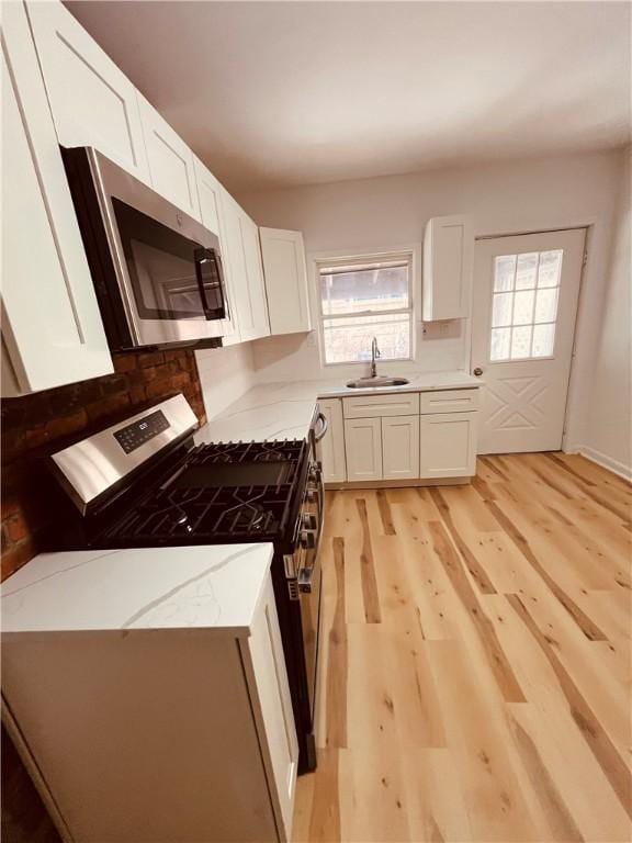 kitchen with sink, stainless steel appliances, light stone counters, white cabinets, and light wood-type flooring