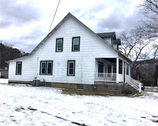 snow covered property with central AC and covered porch