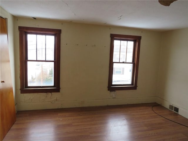 unfurnished room featuring visible vents, a healthy amount of sunlight, and wood finished floors