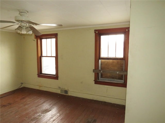 empty room featuring a wealth of natural light, visible vents, wood-type flooring, and crown molding