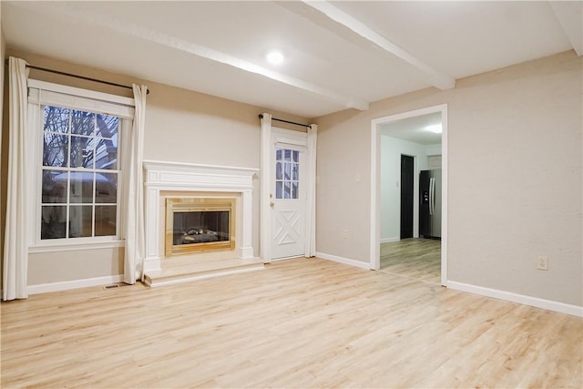 unfurnished living room featuring beamed ceiling, a premium fireplace, and light hardwood / wood-style flooring