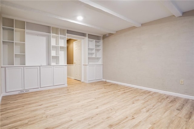 empty room featuring beamed ceiling and light wood-type flooring