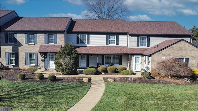 view of front of home with a front yard, a porch, brick siding, and a shingled roof