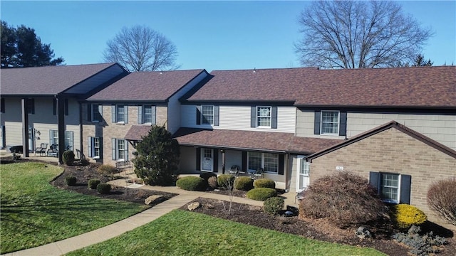 view of front of house featuring brick siding, covered porch, a front yard, and roof with shingles