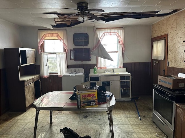 kitchen featuring sink, wood walls, stainless steel range with gas stovetop, ceiling fan, and washer / clothes dryer