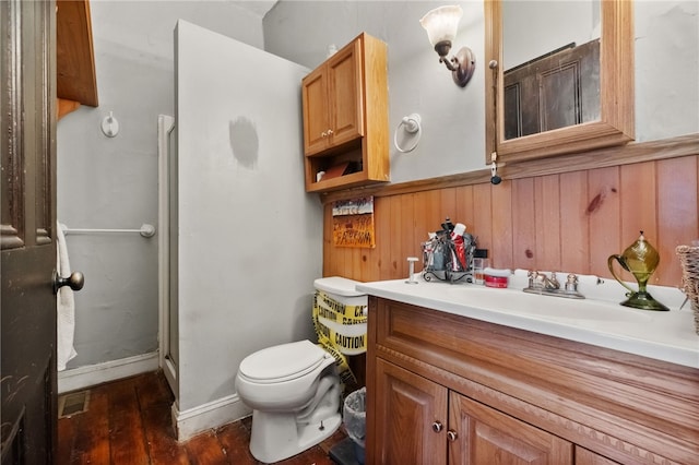 bathroom with wood walls, a shower with shower door, hardwood / wood-style flooring, vanity, and toilet