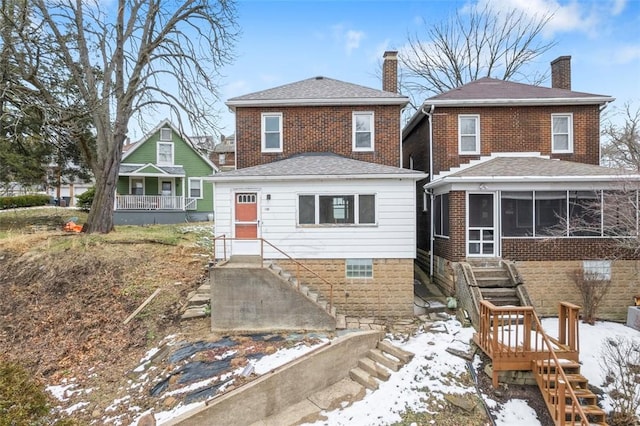 snow covered back of property with a sunroom