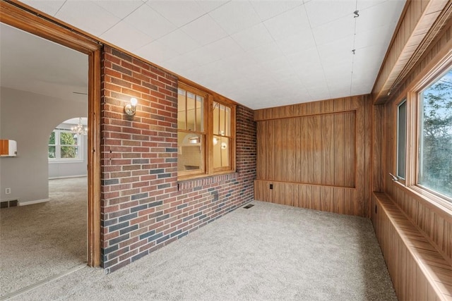 spare room with radiator, light colored carpet, wood walls, and brick wall