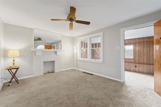 unfurnished living room with a fireplace, light colored carpet, ceiling fan, and wood walls