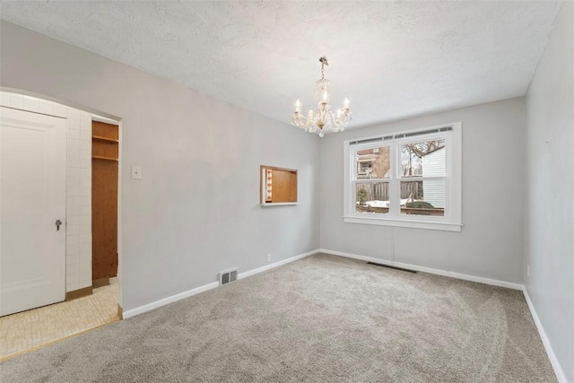 empty room featuring an inviting chandelier, a textured ceiling, and carpet