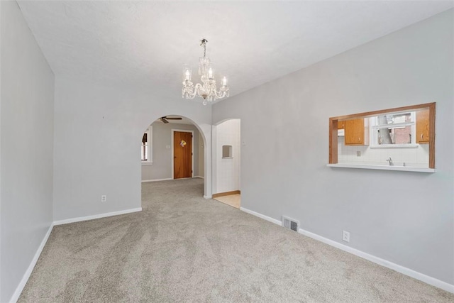 empty room with light colored carpet and a notable chandelier