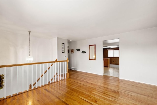 empty room with wood-type flooring and a chandelier