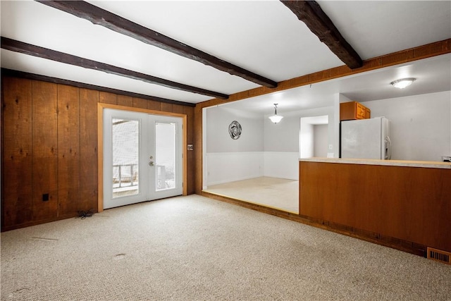 carpeted spare room featuring french doors, beam ceiling, and wood walls