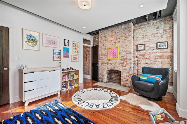 sitting room with brick wall, a brick fireplace, and light wood-type flooring