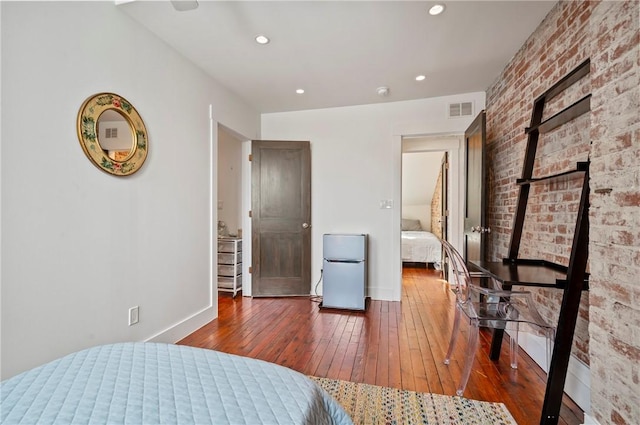 bedroom featuring stainless steel refrigerator, brick wall, and dark hardwood / wood-style floors