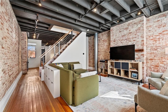 living room with a towering ceiling, brick wall, rail lighting, and light wood-type flooring