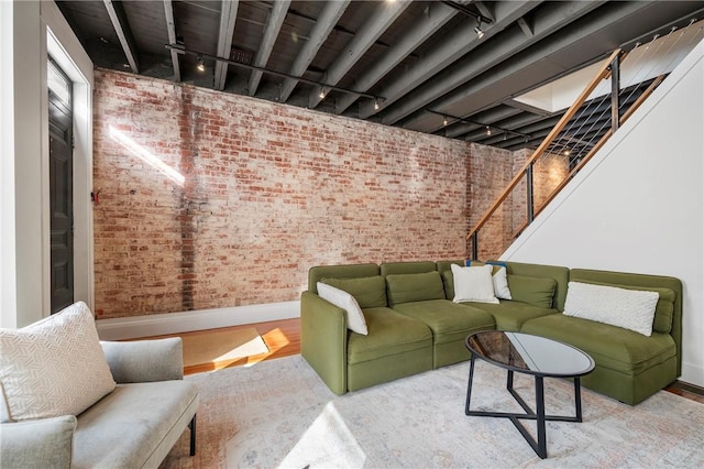 living room featuring light hardwood / wood-style flooring, rail lighting, and brick wall