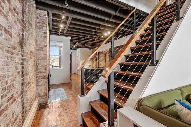 stairway with wood-type flooring and brick wall