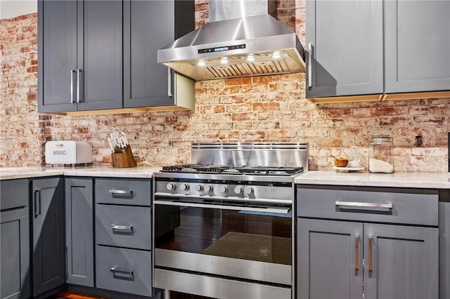 kitchen with gas range, gray cabinets, brick wall, light stone countertops, and exhaust hood