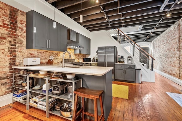 kitchen with sink, high quality fridge, kitchen peninsula, brick wall, and wall chimney range hood