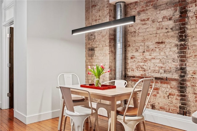 dining space with hardwood / wood-style flooring and brick wall