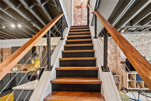 staircase featuring brick wall, rail lighting, and wood-type flooring