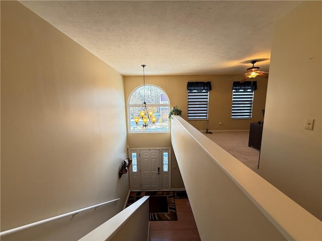 stairway featuring ceiling fan with notable chandelier and a textured ceiling