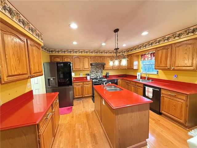 kitchen with sink, decorative light fixtures, light wood-type flooring, appliances with stainless steel finishes, and an island with sink