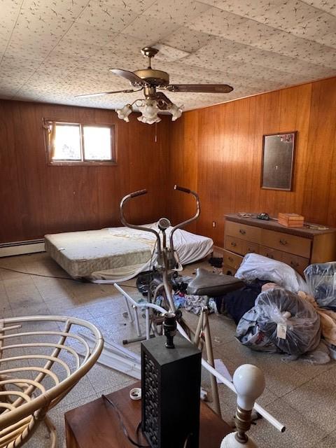 bedroom featuring baseboard heating, ceiling fan, and wood walls