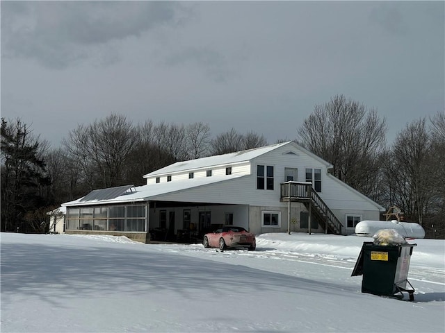 snow covered rear of property with a sunroom