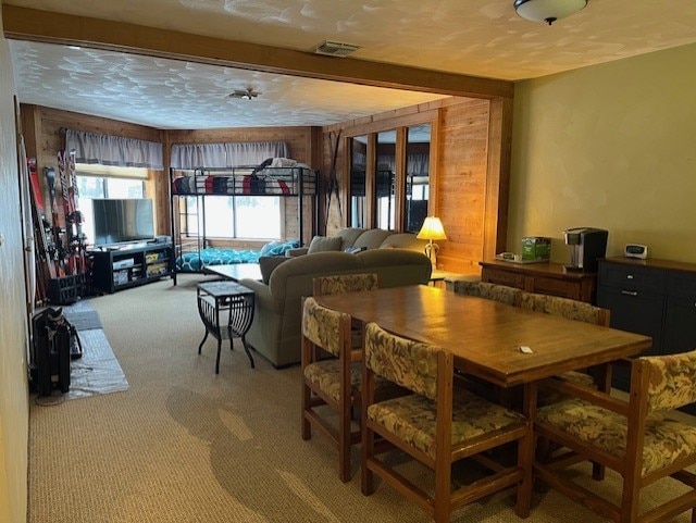 dining space with a textured ceiling, carpet, and wood walls