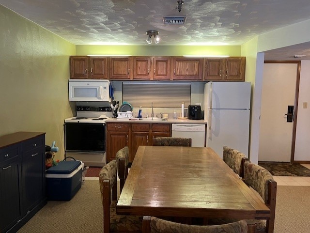 kitchen with sink, light carpet, a textured ceiling, and white appliances