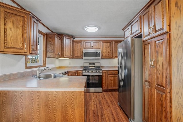 kitchen featuring stainless steel appliances, kitchen peninsula, sink, and light hardwood / wood-style flooring