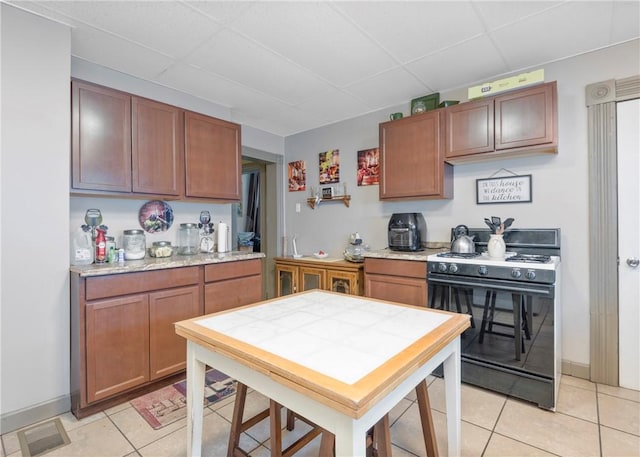 kitchen with light tile patterned floors, a drop ceiling, and range with gas cooktop