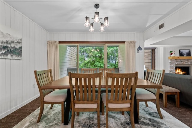 carpeted dining room with an inviting chandelier, a brick fireplace, and wood walls