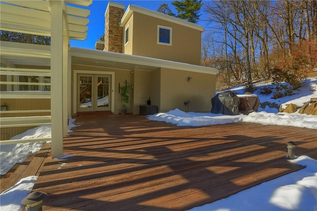 snow covered rear of property with french doors and a deck