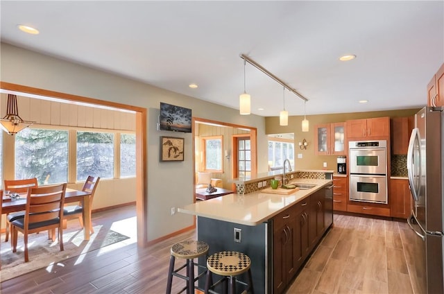 kitchen featuring appliances with stainless steel finishes, tasteful backsplash, sink, hanging light fixtures, and light hardwood / wood-style floors